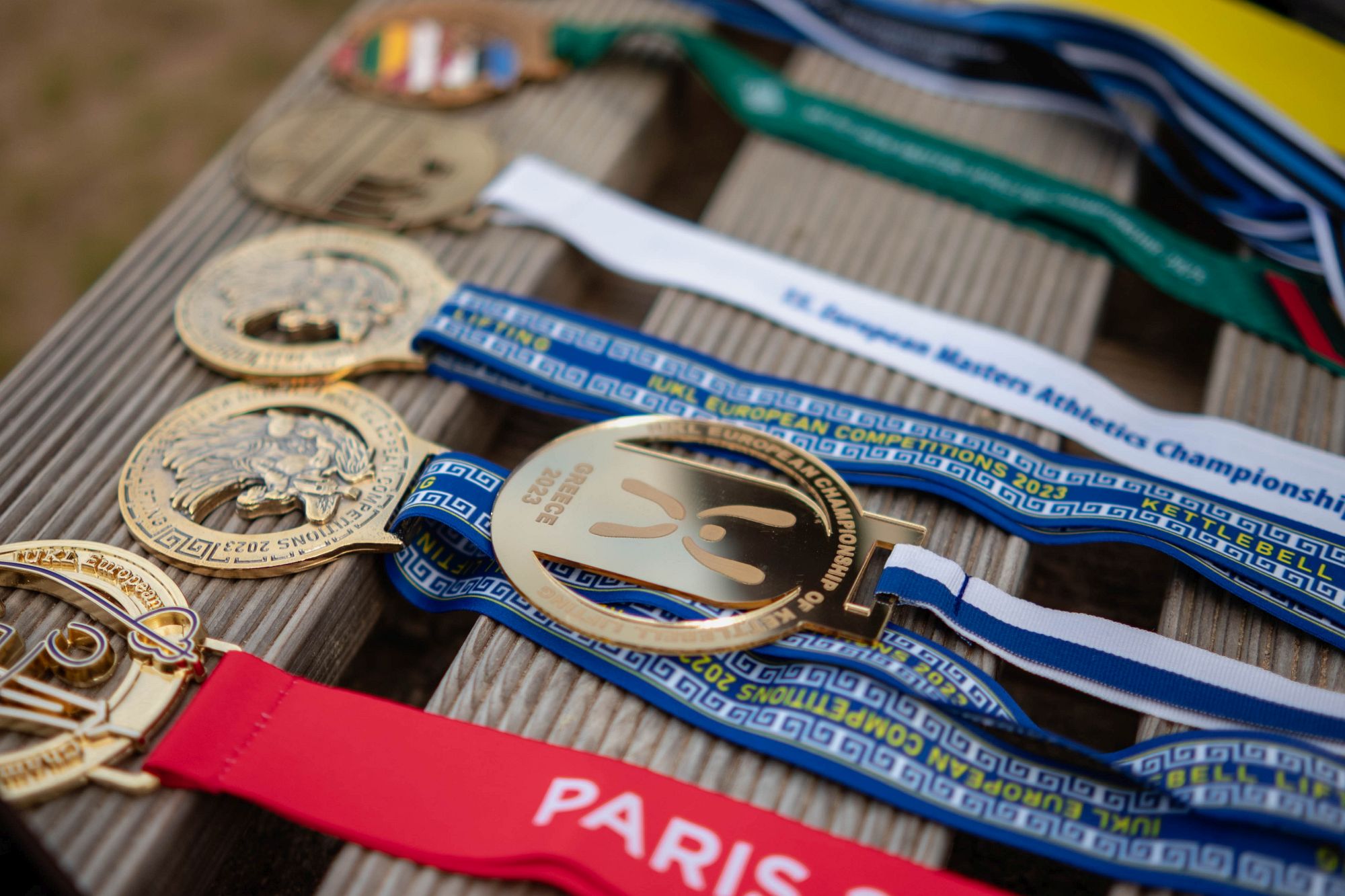 Медали разложены на деревянной поверхности: ленты, надписи European Championships, Paris, Estonia, Latvia.